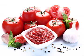 Ketchup in bowl with basil leafs and garlic on wooden table