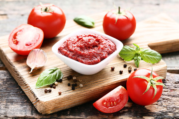 Ketchup in bowl with basil leafs and pepper on wooden table