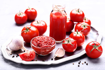 Tomato juice in glass bottle with ketchup and garlic on grey wooden table