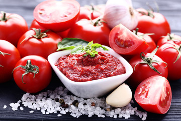Ketchup in bowl with basil leafs and salt on black wooden table