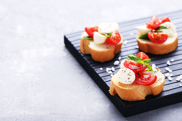Bruschetta with mozzarella, tomatoes and basil leafs on wooden cutting board