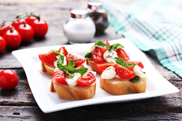 Bruschetta with mozzarella, tomatoes and basil leafs on grey wooden table
