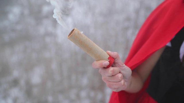 A woman holds a smoke grenade that slowly burns down and goes out during the day in the snow