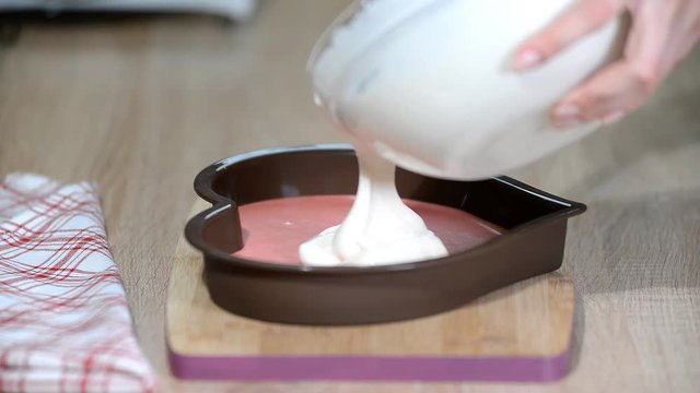 Pouring vanilla mousse into heart shaped molds. Confectioner making mousse cake in the kitchen.