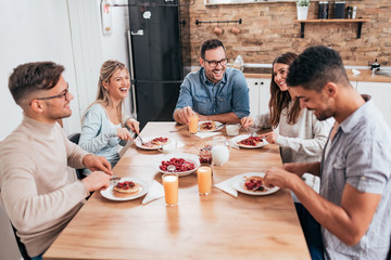 Friends sitting around wooden table, eating dessert and having fun.