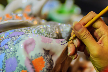 Close up hand of Thai woman artist during painting the masterpiece of Benjarong patterns, the famous thai 5- colored porcelain ceramic wares.