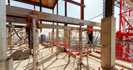 high building under construction with workers in the construction site on supports wearing safety...