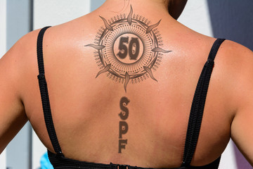 sunburned back of girl in a black bikini with a tattoo of the sun. SPF 50 a symbol. design of...