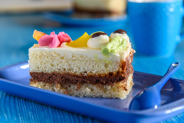 Puff biscuit cake with custard on a ceramic plate, behind the cup of coffee, photographed on a blue wooden background.