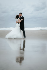 Adorable wedding couple walking along the beach, reflecting in the water.