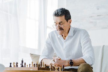 senior man with mustache looking at chess board at home