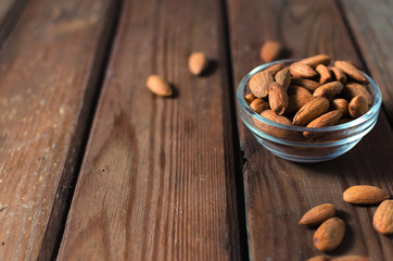Almonds in a glass bowl on grained wood background. Selective focus.
