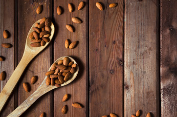 Obraz na płótnie Canvas Almonds in a glass bowl and wooden spoons on grained wood background. Top view.