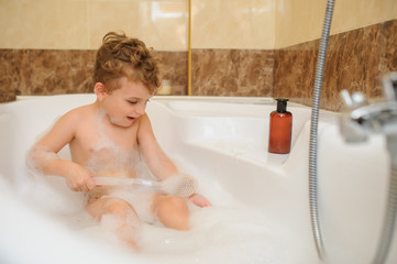Little boy washing and playing in bathtub with foam and soap bubbles