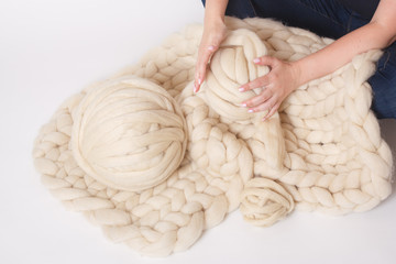 Blanket made of Merino wool and yarn balls on white background. Women's hands holding a ball.