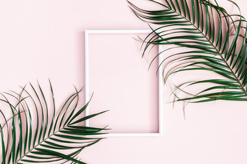 Summer composition. Tropical palm leaves, white photo frame on pastel pink background. Summer concept. Flat lay, top view, copy space
