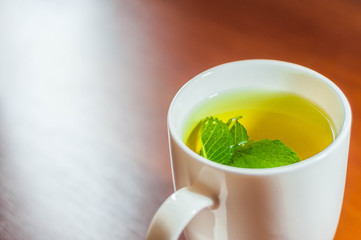 Green tea in a white cup with mint leaves on a wooden table background. Winter avitaminosis before spring.