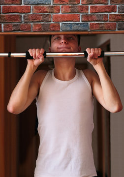 Young Man Executing Exercise Pulling Up On Horizontal Bar At Home