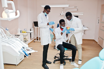 Three african american male doctors colleagues in dental clinic with an apple.