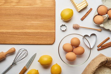 top view of empty wooden cutting board and bakery ingredients on grey background