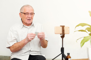 Smiling eldery man looking at camera making video blog or call at home sitting on sofa dating...