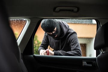 Car thief in a balaclava is trying to break into a car
