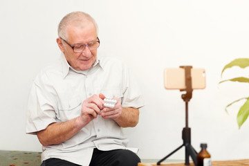 Smiling eldery man looking at camera making video blog or call at home sitting on sofa dating...