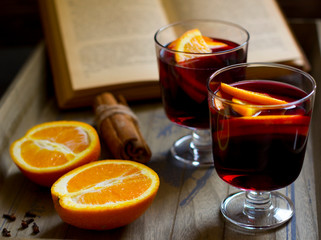 Mulled wine, book, orange and cinnamon on dark wooden background