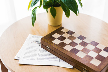 wooden chess board near newspaper and plant on coffee table