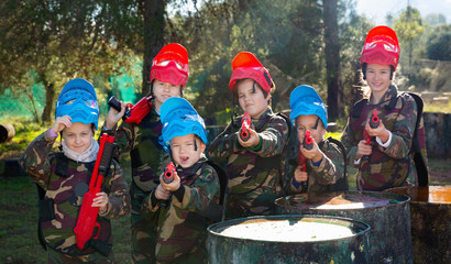 Friendly group of children paintball players in camouflage posing with guns on paintball playing...