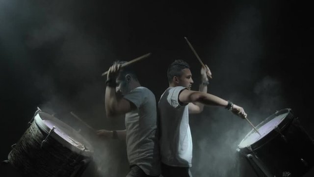 Two people play on color drums on the black background