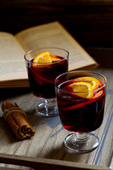 Mulled wine, book, orange and cinnamon on dark wooden background
