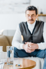 selective focus of pills and glass of water with senior man on background