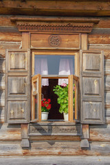 vintage window with shutters in an old wooden peasant house, with blooming geranium on the windowsill