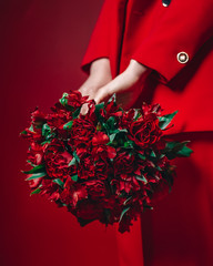 young woman in red suite holds a bouquet of roses and alstroemerias on red background