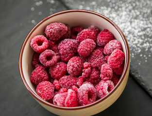 Bowl of fresh frozen raspberries fruit, closeup top view