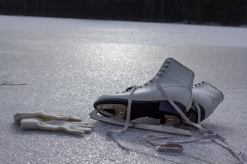 Women's skates and white gloves lying on the ice. Skating on the pond. Winter sports, relaxation.