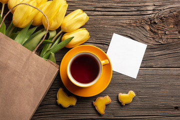 Easter gingerbread cookies, cup of tea on wooden table and yellow tulips. Greeting card. Top view with copy space.