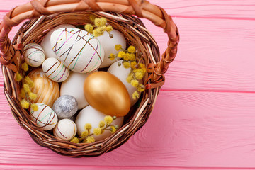 Woven basket with Easter eggs. White, gold and styrofoam decorated eggs with pussy willow in basket. Happy Easter holidays.