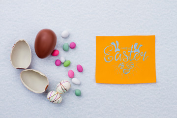 Broken chocolate egg on light background. Styrofoam Easter eggs and colorful candies. Easter greeting card. Easter present for kids.