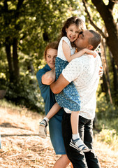 Happy parents kiss and hug a laughing daughter in the forest for a walk