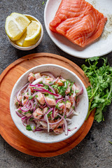 CHILEAN SALMON SEVICHE. Fresh raw salmon marinaded with purple onion, coriander in lemon juice. Ceviche and ingredientes on gray background. Top view
