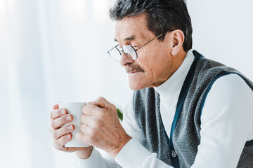 senior man in glasses holding cup with drink in hands