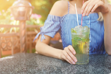 Young woman with glass of tasty lemonade at table in cafe, outdoors. Natural detox drink