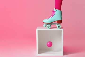 Woman wearing vintage roller skate and storage cube with ball against color background, closeup....