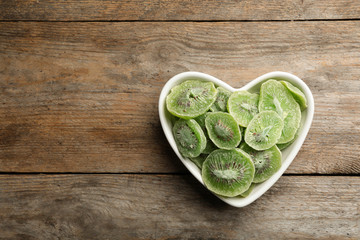 Bowl of dried kiwi on wooden background, top view with space for text. Tasty and healthy fruit