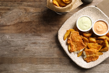 Fototapeta premium Plate with British traditional fish and potato chips on wooden background, top view. Space for text