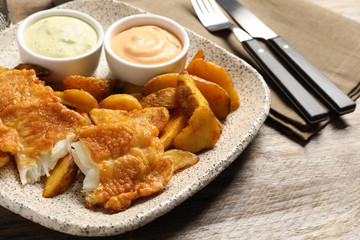 Plate with British traditional fish and potato chips on wooden table, closeup