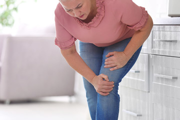 Senior woman suffering from knee pain in kitchen