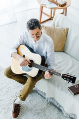 overhead view of cheerful senior man playing acoustic guitar in living room